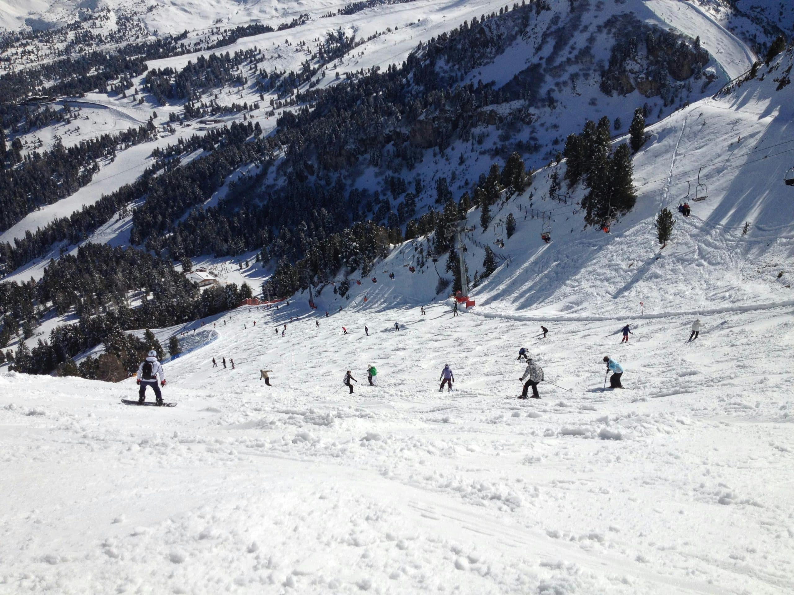 Views of a snow-capped mountain with people skiing.