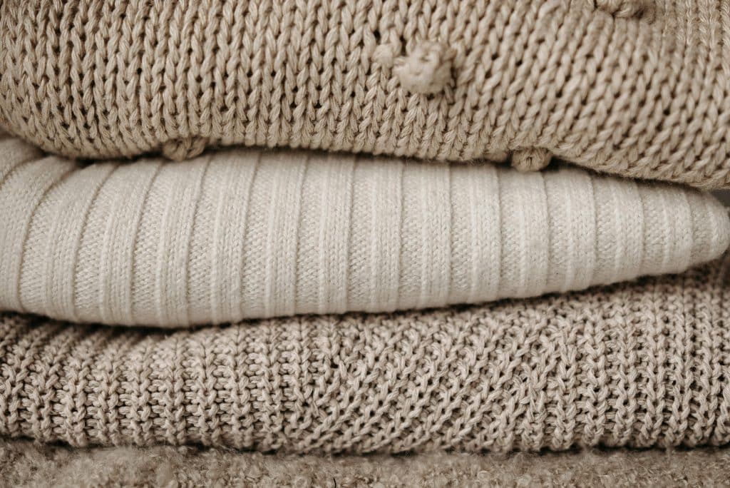 Several woollen jumpers, one on top of the other, in shades of brown and beige.