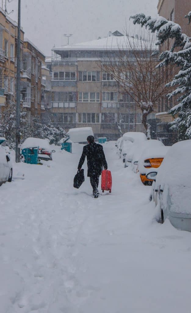 Hombre caminando en una calle llena de nieve con las maletas en la mano