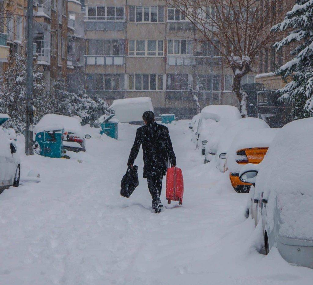 Hombre caminando en una calle llena de nieve con las maletas en la mano