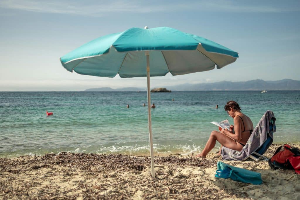 Mujer sentada en la playa bajo una sombrilla
